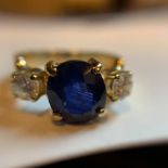A SAPPHIRE AND DIAMOND THREE STONE RING. THE CENTRAL SAPPHIRE BEING A VIOLET BRIGHT MID TO DARK BLUE