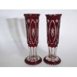 Pair of overlaid ruby glass vases with an oval cut panel design on a circular foot, each 24cms tall