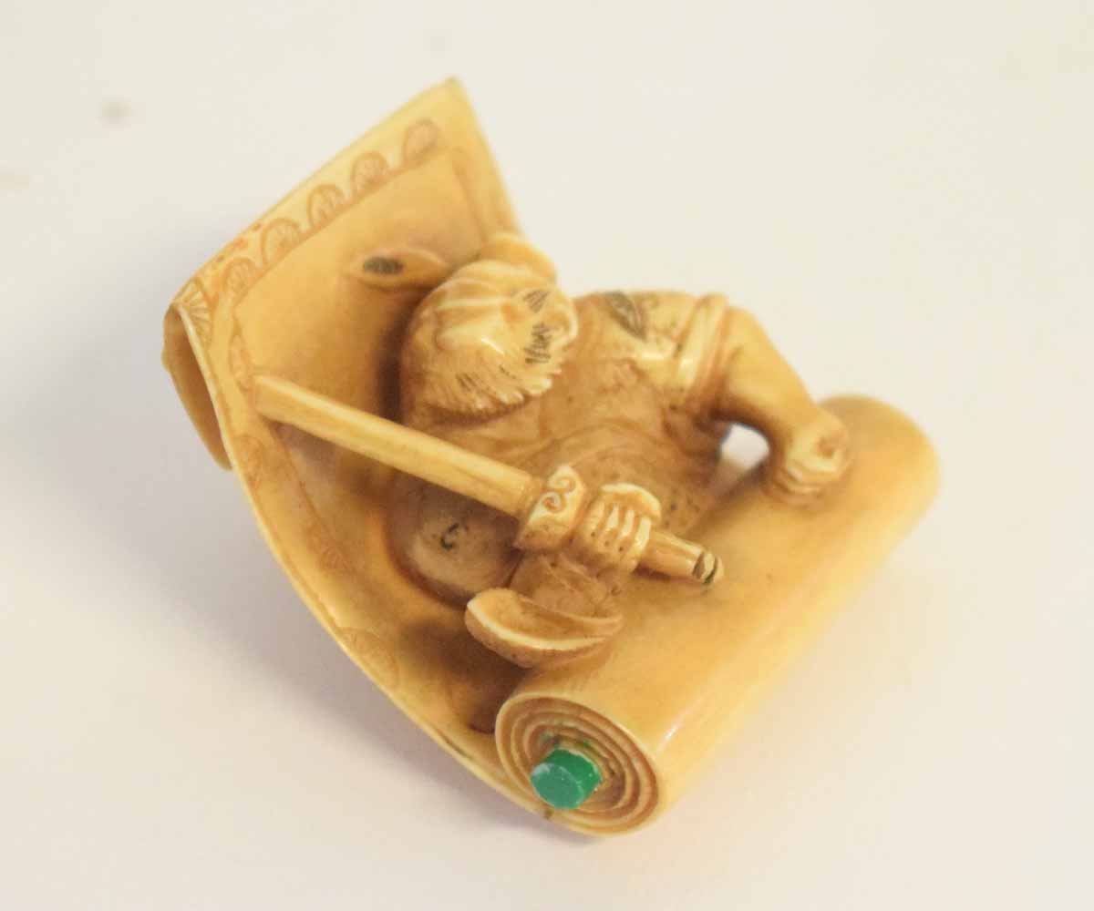 Japanese ivory netsuke carved with Shoki chasing an Oni over a scroll