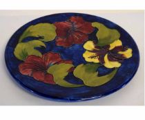 Moorcroft circular platter, Hibiscus pattern to a blue ground, 30cms diam, green painted mark,