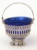 George V swing handled sugar basket, with pierced handle and body on spreading foot with fitted blue