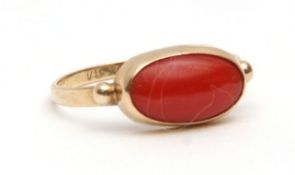 Yellow metal and coral ring, the oval cabochon coral in a bezel setting, having beaded shoulders