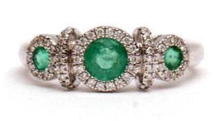 Modern precious metal emerald and diamond ring, a design of three graduated circular cut emeralds,