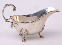 George V sauce boat of polished form with beaded rim and flying C-scroll handle on three feet,