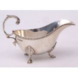 George V sauce boat of polished form with beaded rim and flying C-scroll handle on three feet,