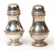 Two George V pepper casters, each of girdled baluster form with pierced and pull off covers on