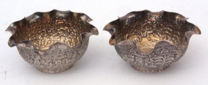 Two various Indian white metal small bowls each with crimped rims and profusely embossed bodies