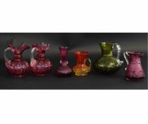 Collection of six glass ewers, predominantly cranberry coloured, together with one green ewer,