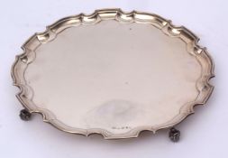 George V silver salver with shaped rim, polished field and raised on four cast and applied scrolling