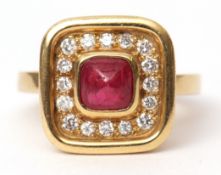 18ct gold ruby and diamond ring, the square panel design with a central cabochon ruby, collet set,