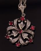 9ct white gold ruby and diamond openwork pendant and chain, a circular shaped design of scrolls,