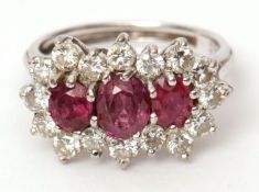 Precious metal ruby and diamond cluster ring, features three graduated oval cut rubies, surrounded