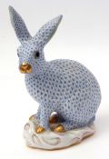 Herend model of a rabbit decorated in blue enamel with black glass eyes, seated on a rocky mound,