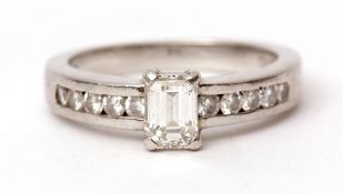Precious metal emerald cut diamond ring, the central diamond raised between channel set diamond