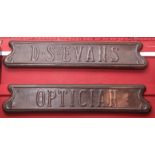 Two oak backed copper name wall plaques "D S Evans/Optician", each in the Art Nouveau manner with