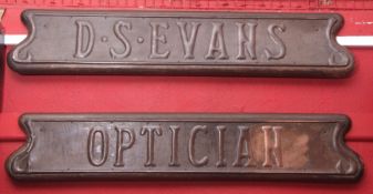 Two oak backed copper name wall plaques "D S Evans/Optician", each in the Art Nouveau manner with