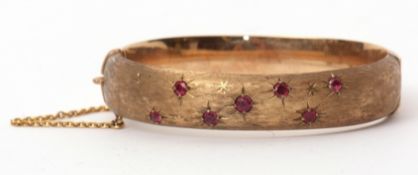 9ct gold and ruby hinged bracelet, the textured front with seven circular cut rubies in star