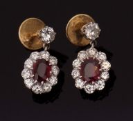 Pair of ruby and diamond pendant earrings, the oval shaped ruby surrounded by a cluster of brilliant