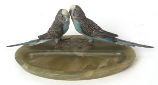 Early 20th century onyx ashtray of oval form, crested with two cold painted budgerigars, 11cms high
