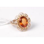 A citrine ring, the oval citrine in a rubover mount with decorative scrolled surround,