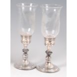 A pair of modern silver candle holders, each having wheel engraved glass shades with silver bases,