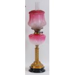 A late Victorian brass pedestal oil lamp, having a cranberry tinted and acid etched shade,