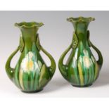 A pair of Art Nouveau twin handled pottery vases, each underglazed in tones of green,