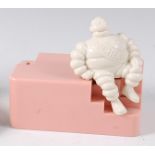 A Michelin bakelite employees money-box, modelled as a seated Mr Bibendum to pink base, h.13cm, w.