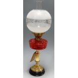 An early 20th century oil lamp, having etched opalescent globular shade to a red tinted glass font,