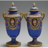 A pair of Noritake pedestal urns and covers, each on a blue ground with a reserve of hand-painted