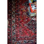 A Persian woollen red ground rug having central lozenge decoration within trailing tramline