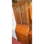 A 1930s oak bureau bookcase, having twin lead glazed upper doors over three long lower drawers, with