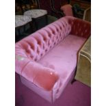 A late Victorian pink upholstered buttonback three-seater Chesterfield, raised on bun supports, w.