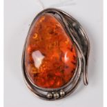 An amber brooch, the large oval amber with Arts & Crafts style border and mount in unmarked white