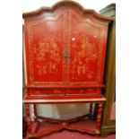 A contemporary red lacquered dome-top two door cabinet on stand, having twin short drawers,