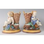 A pair of Victorian Wedgwood majolica vases, each modelled as a cherub seated against a basket, on