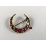 A late 19th / early 20th Century crescent moon brooch, set with diamonds and red stones, on yellow-