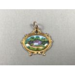 An enamelled 9ct gold fob, painted in depiction of a country cottage in an idyllic rural setting,