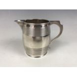 A George IV silver barrel form milk jug, having an engraved armorial crest and monogram, SC, London,