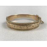 A 9ct gold hinged bangle, the face foliate engraved and edged in an open wirework frame, with
