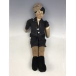 A 1920s cloth doll, modelled as a young boy, wearing cloth cap, a black short suit and velvet boots,