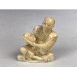 A Meiji Japanese small ivory okimono depicting a figure sat holding a noh or similar mask, inset