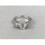 A vintage Art Deco three-stone diamond and platinum ring, having a central baguette-cut stone of