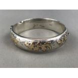 An Elizabeth II silver hinged bangle, the face having applied yellow-metal foliage and birds,