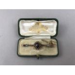 An early 20th Century garnet and pearl open bar brooch, having a central oval-cut stone of