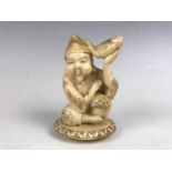 A small Japanese carved marine ivory sculpture of a figure sat holding a carp, mid 20th Century, 7.5