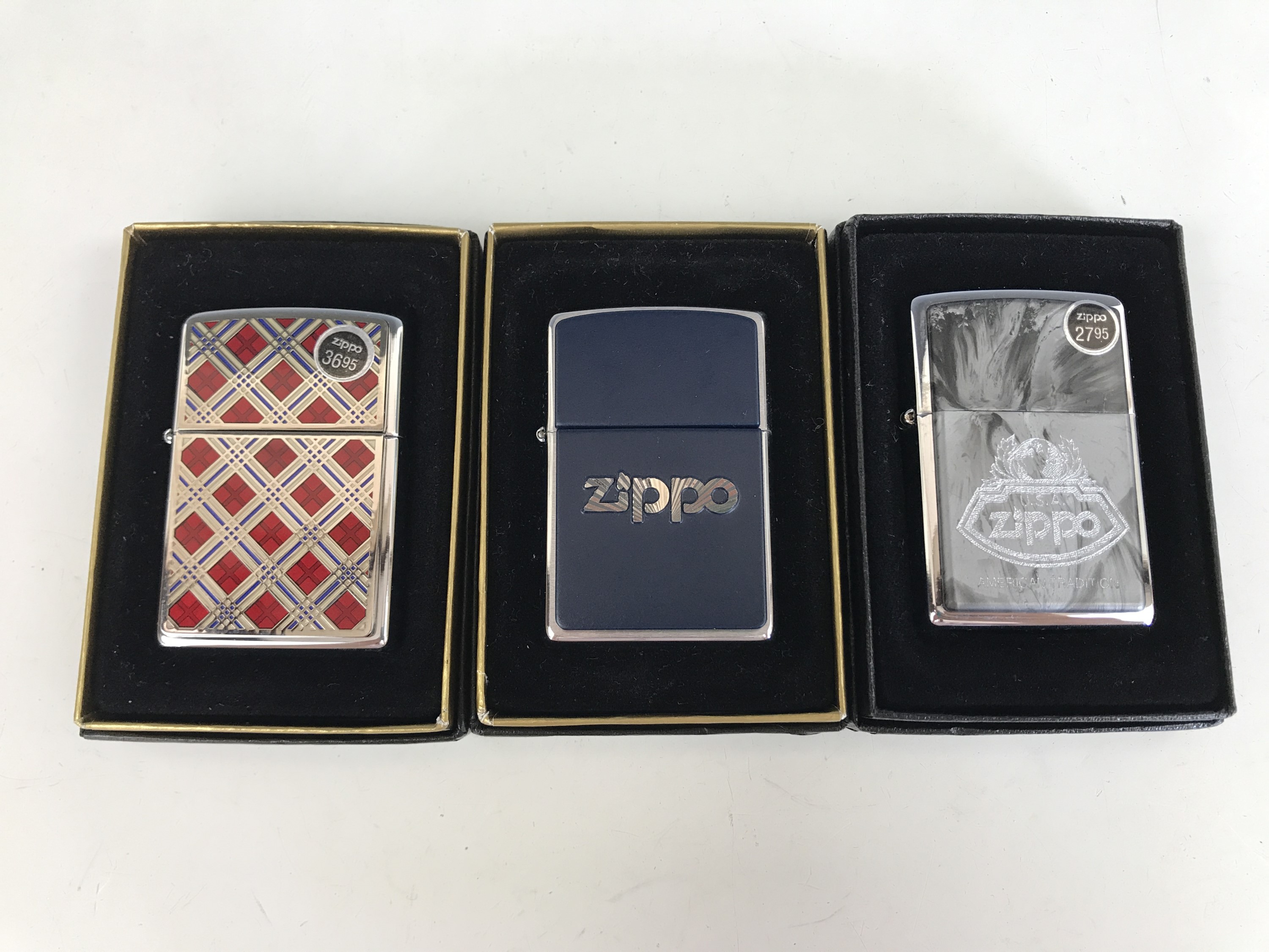 Three cased Zippo lighters, including No. 20429 Cherry Plaidness Emblem, No. 200 Blue and Chrome,