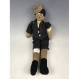 A 1920s cloth doll, modelled as a young boy, wearing cloth cap, a black short suit and velvet boots,