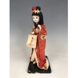 A vintage Japanese figurine of a Geisha, wearing woven and printed cotton robes, over a black