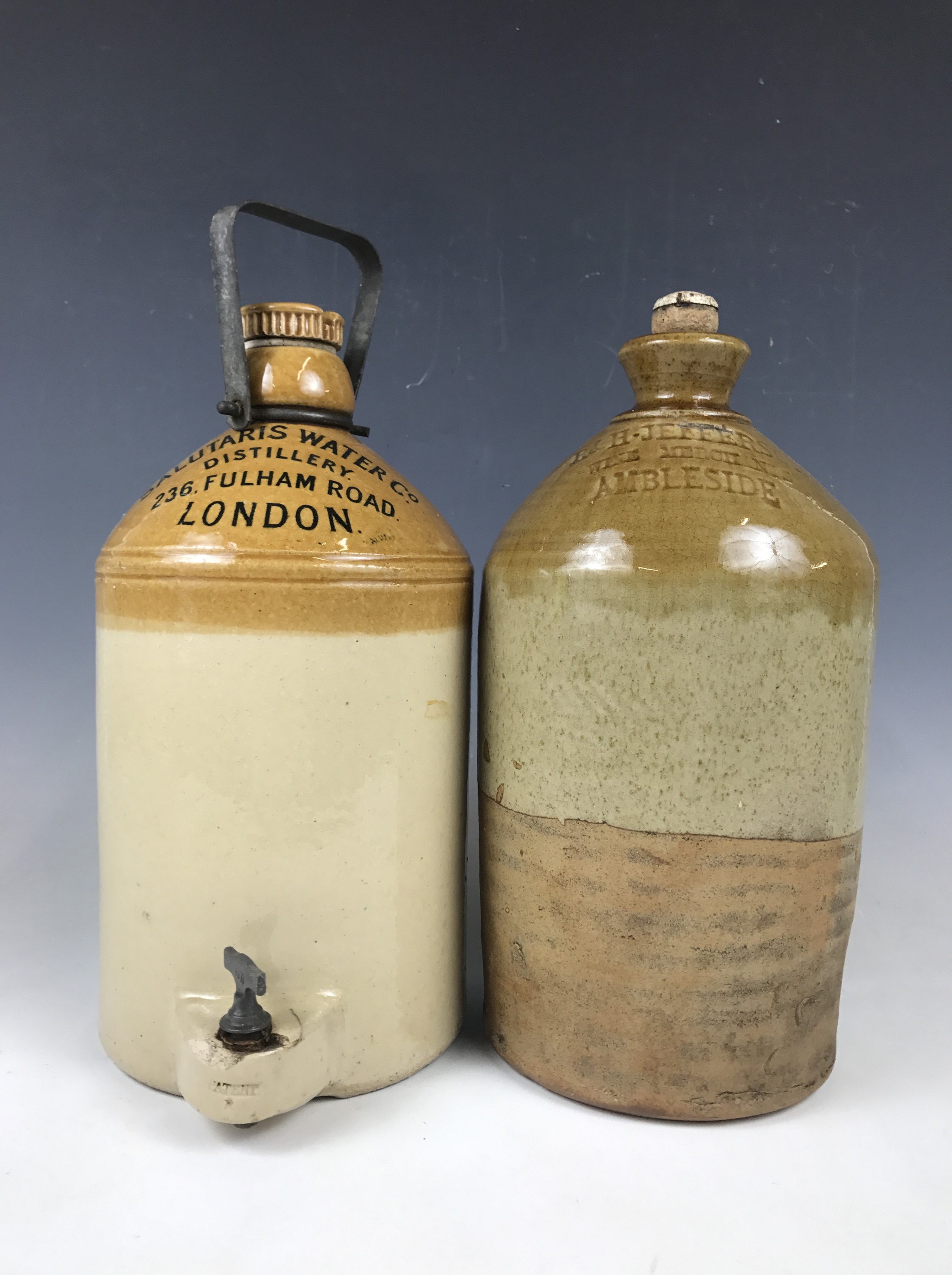 A stoneware flagon with tap, printed "Salutaris Water Co Distillery, 236 Fulham Road, London",